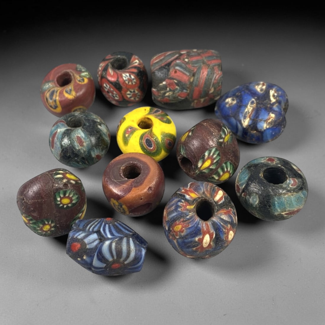 Antique Venetian Glass Beads - 12 Pieces, 56FX: This set of 12 antique Venetian glass beads features diverse hand-formed shapes including spherical, barrel, and irregular forms, crafted from polychrome glass with intricate mosaic and cane-work patt