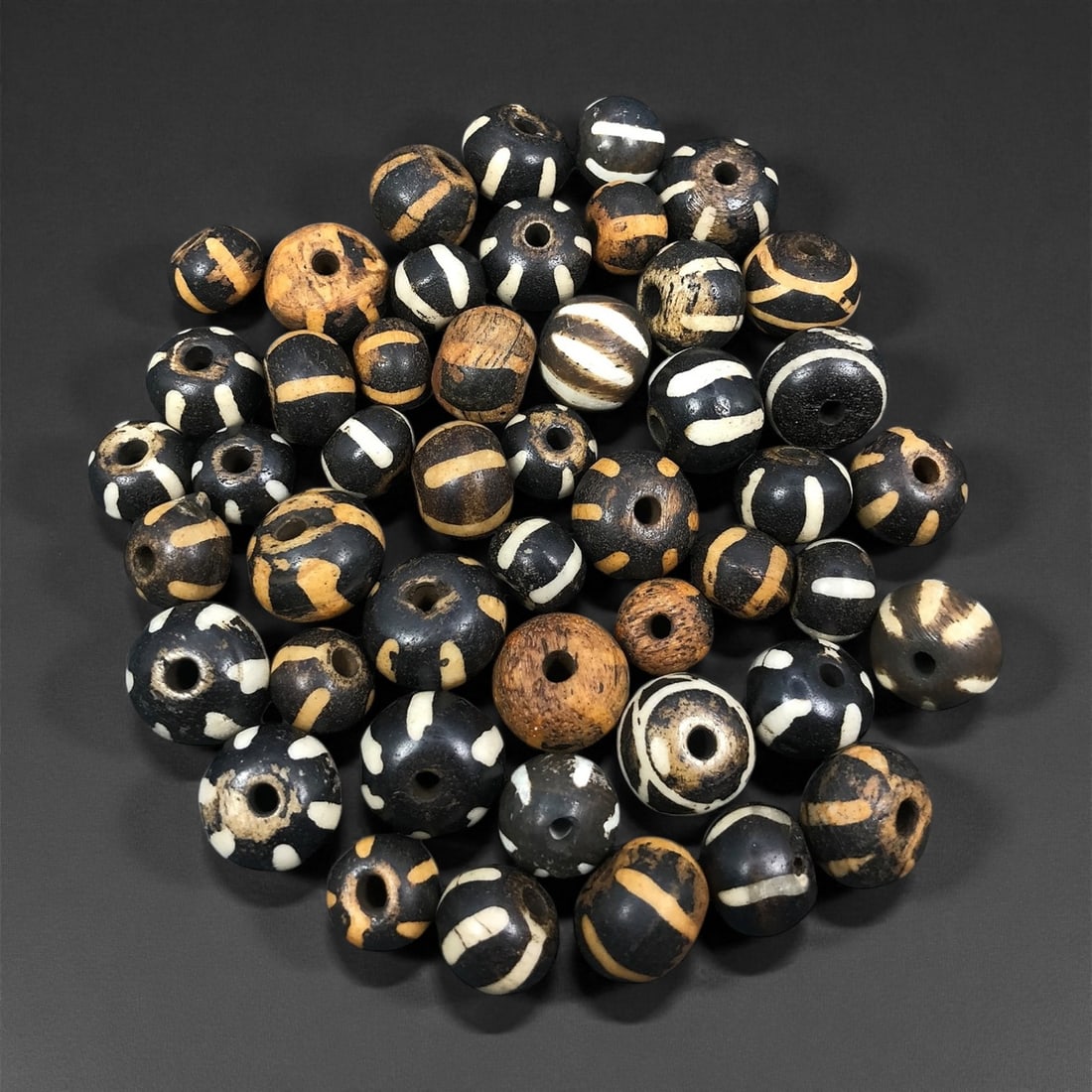 A Group of Burmese Pumtek Wood Beads, 19th-20th Century, 93FS: The group consists of forty-seven spherical beads, carved from wood and treated with a dark surface, overlaid with white and light tan geometric patterns. The beads display a range of consistent motif
