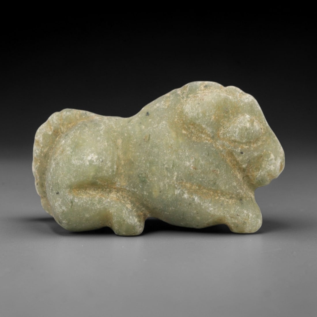 Ancient Serpentine Bovid Amulet - Near Eastern Animal Figure, 73ZW: This amulet is carved from mottled pale green serpentine, depicting a recumbent bovid (ox/bull) with subtle incised details defining the head, horns, and body contours. The creature is rendered in a c