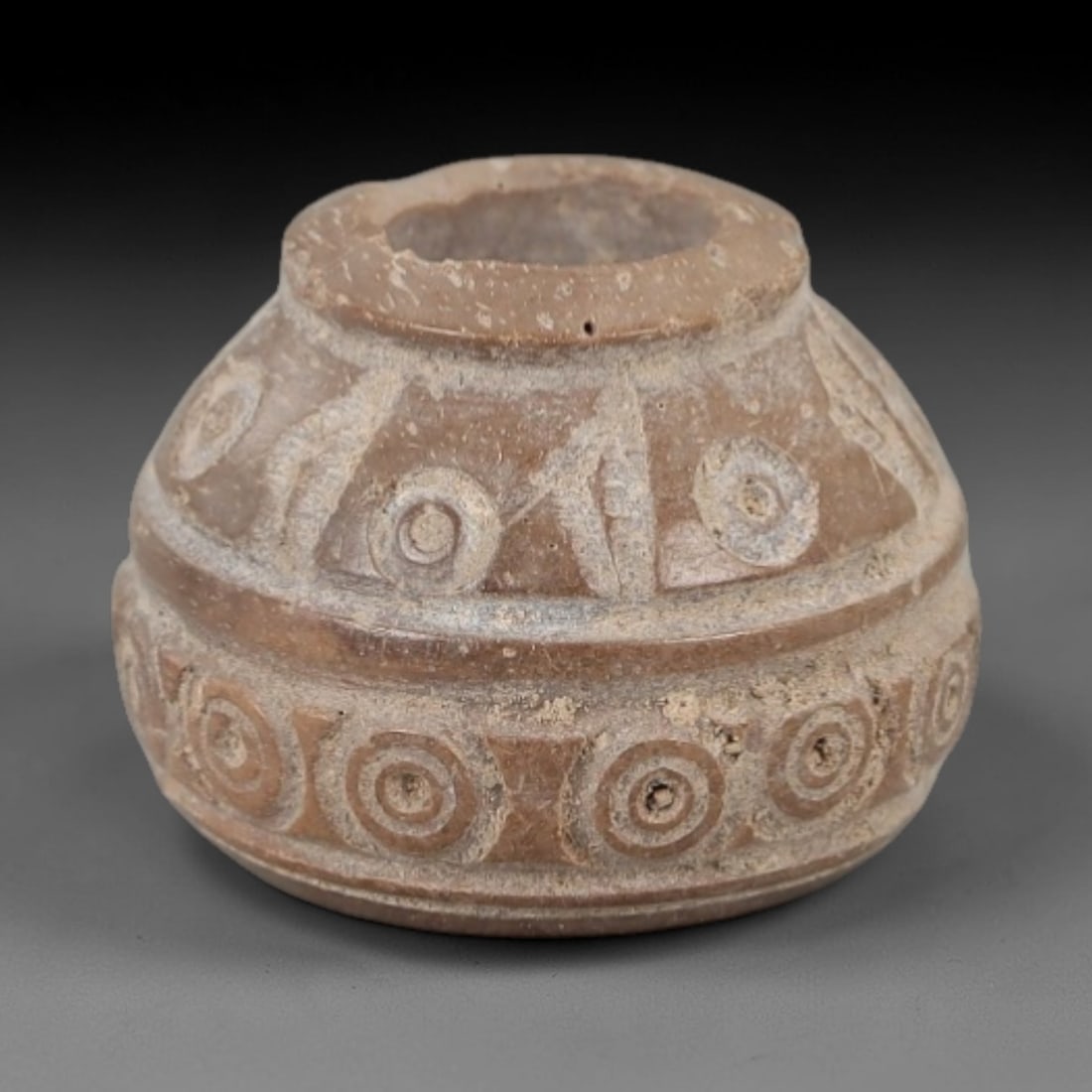 Ancient Stone Spindle Whorl - Near Eastern Concentric Dot Motif, 81XR: This ancient Near Eastern spindle whorl is carved from stone, featuring incised concentric dot patterns radiating from the central perforation. The compact, rounded form is a traditional textile tool