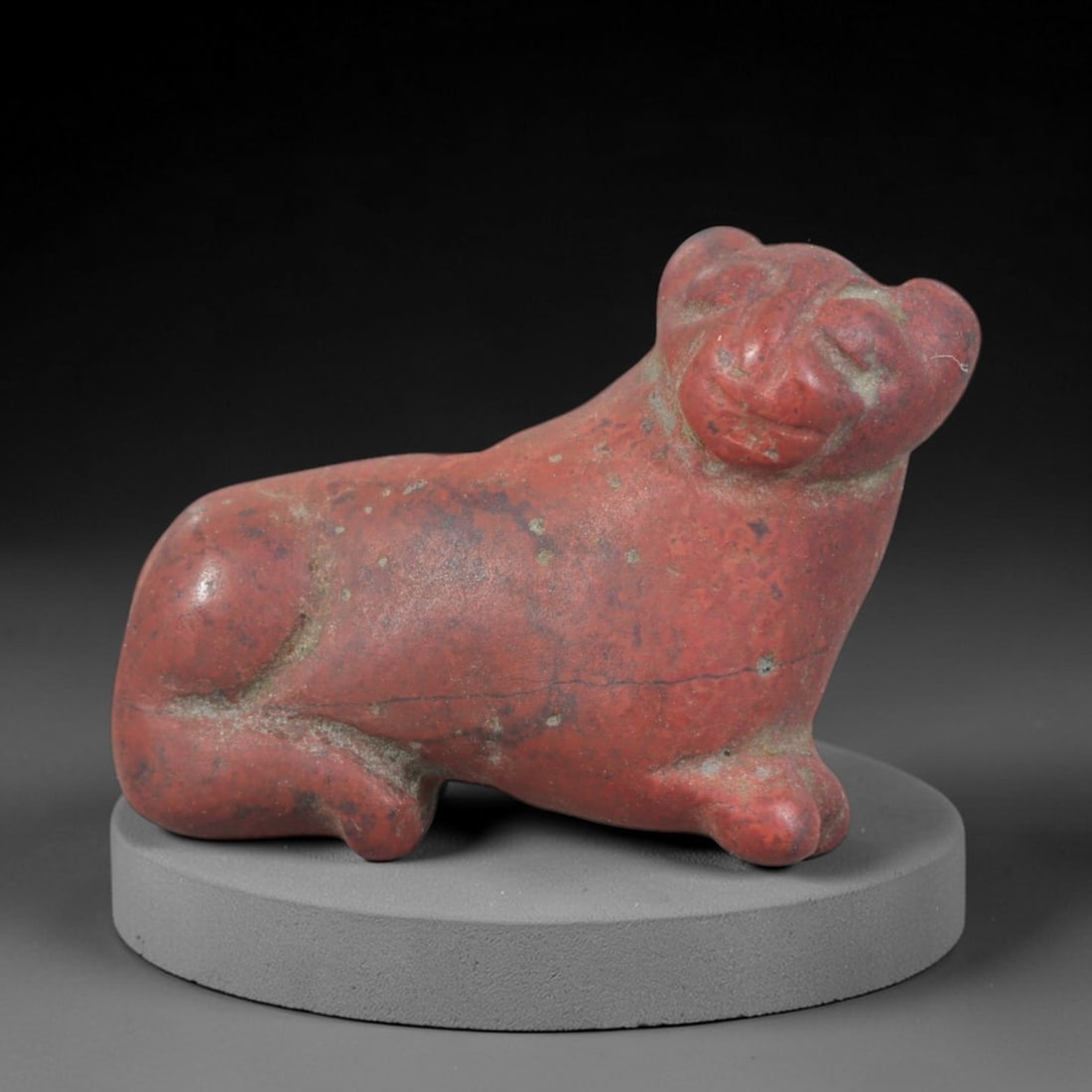 Ancient Stone Recumbent Feline - Near Eastern Figurine, 80AP: This artifact is carved from variegated red stone with a weathered patina and subtle mineral inclusions, exhibiting stylized feline features consistent with ancient Near Eastern stoneworking technique
