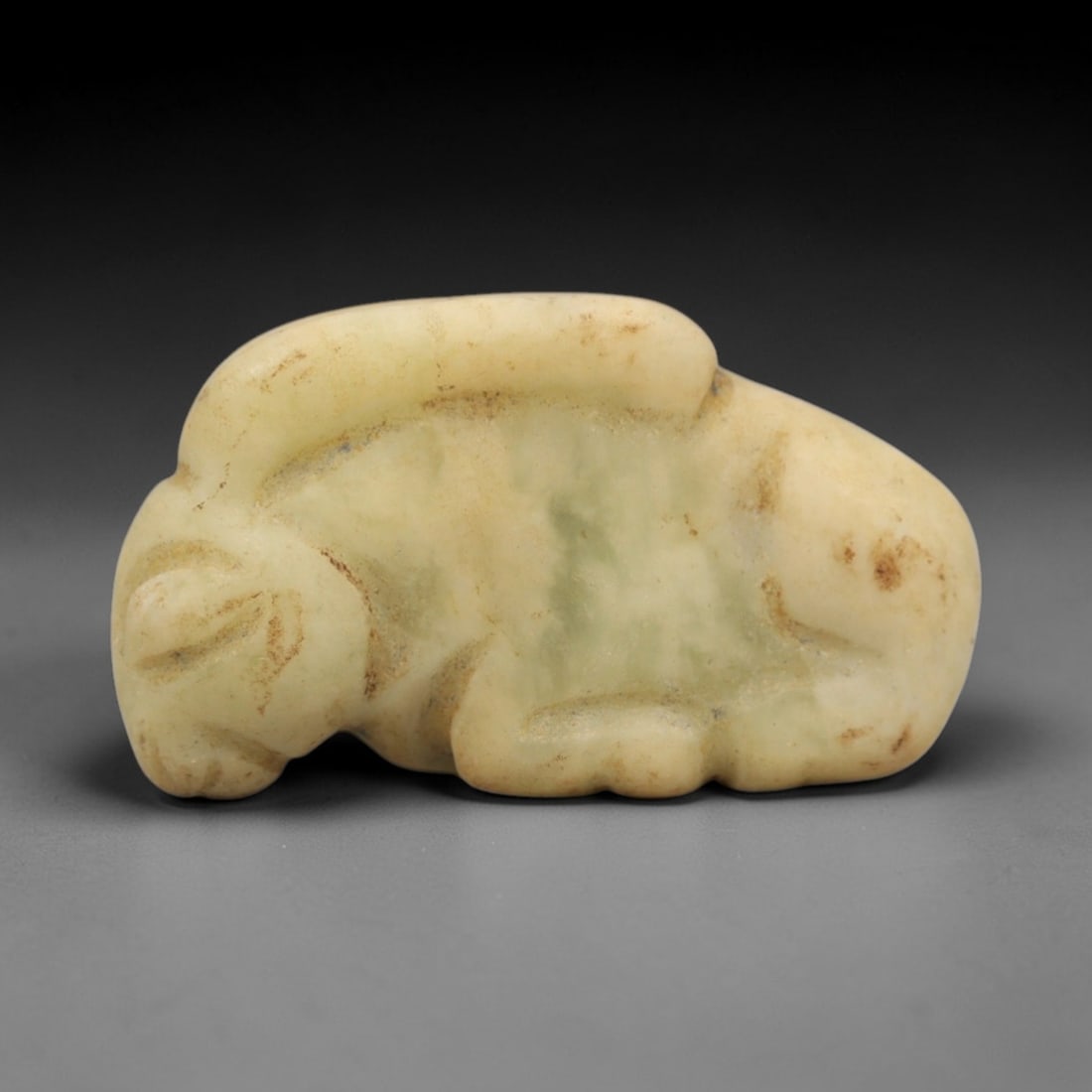 Ancient Serpentine Recumbent Ram Amulet - Near Eastern Animal Figure, 31ZW: This amulet is carved from pale green serpentine with subtle natural veining, depicting a recumbent ram with simplified incised details defining the head, curved horns, and body contours. The creature
