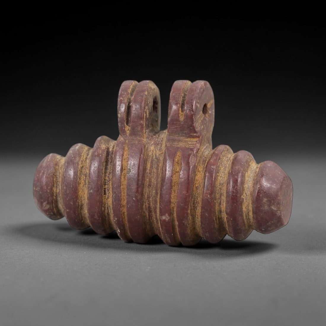 Ancient Jasper Amulet - Near Eastern Ribbed Figure, 66AM: This amulet is carved from jasper, a durable stone favored in ancient Near Eastern protective artifacts, featuring a symmetrical ribbed cylindrical form with dual suspension loops at the top. The hori