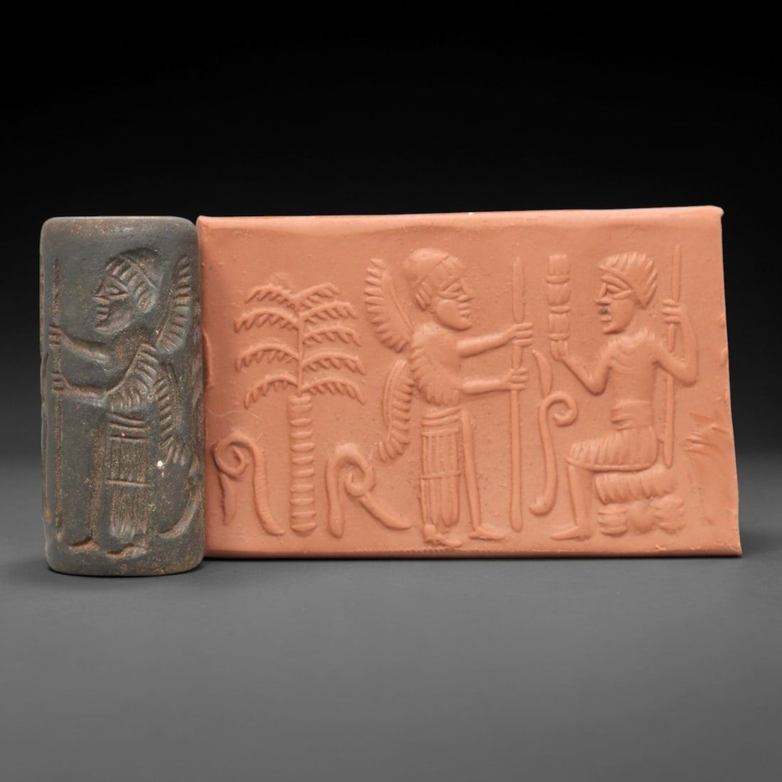 Ancient Steatite Cylinder Seal - Mesopotamian Winged Genius & Ritual Offering Scene, 53AL: Carved from dark, granular steatite, this ancient Mesopotamian cylinder seal depicts a formal ritual offering scene, executed with precise glyptic craftsmanship characteristic of the Neo-Assyrian peri