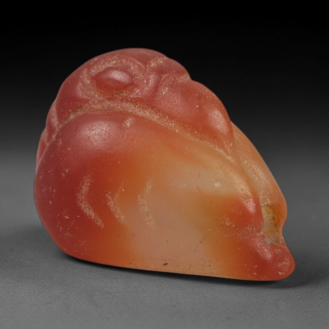 Ancient Carnelian Bird Amulet - Near Eastern Figurine, 49AJ: Carved from warm, translucent orange-red carnelian with natural color gradients, this amulet is formed as a stylized bird with incised linear detailing to define facial features, beak, and body contou
