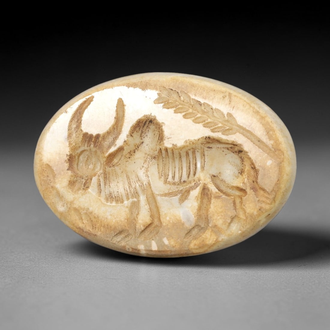 Ancient Stone Bull Intaglio - Near Eastern Amulet, 21AR: This oval intaglio is carved from a pale, creamy stone matrix, featuring a high-relief depiction of a bull in striding pose, with prominent curved horns and incised linear details defining its ribcage