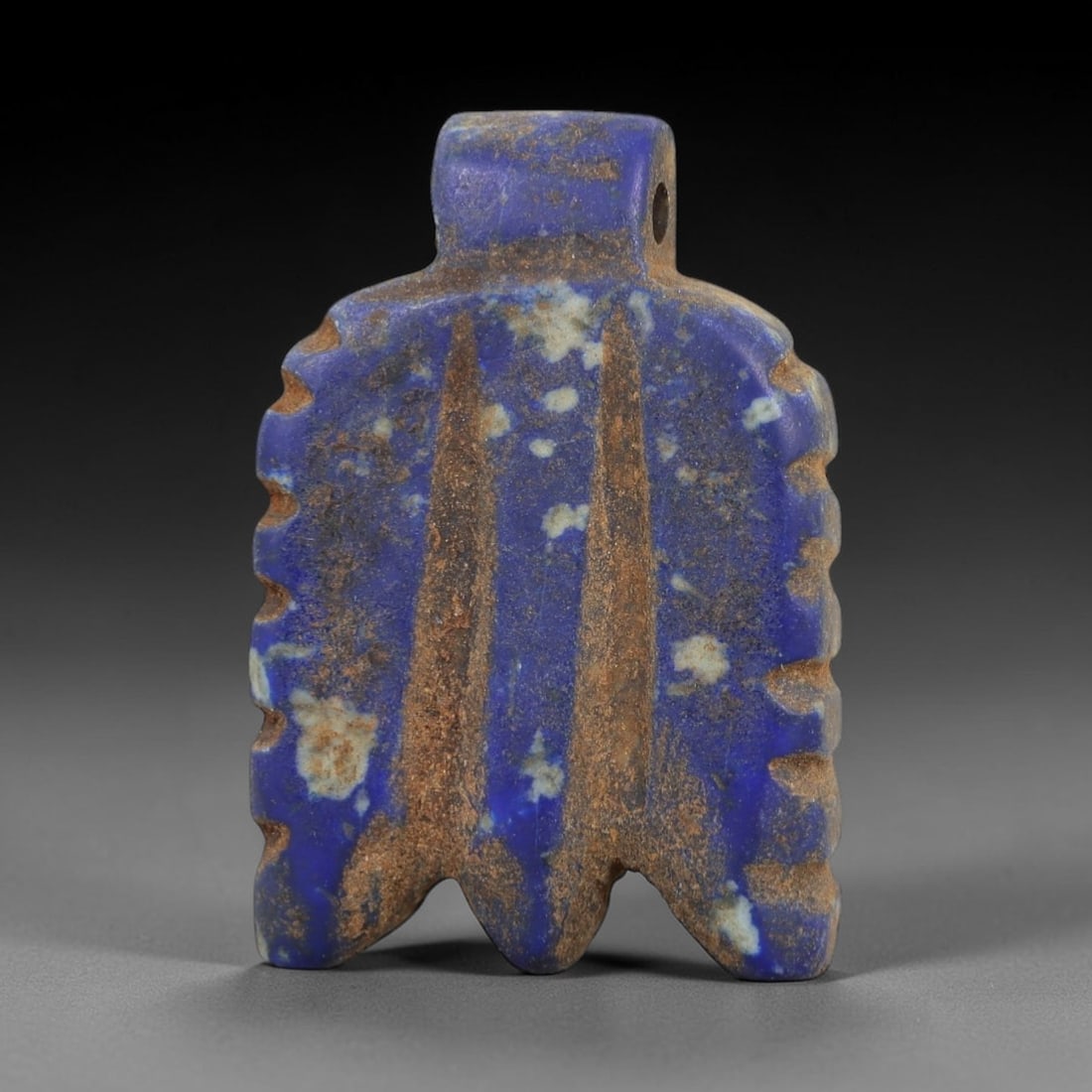 Ancient Lapis Lazuli Amulet - Egyptian Feather Pendant, 21AP: Carved from lapis lazuli, this amulet features a rectangular form with a pierced upper lug, serrated side edges, and two incised vertical feather-like lines defining its central motif, terminating in