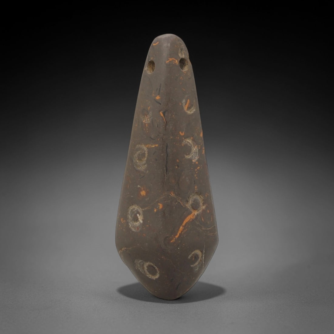 Ancular Stone Amulet - Near Eastern Double-Hole Pendant, 59XP: Carved from dense, fossiliferous stone with distinct orange and grey veining, this amulet features a tapering, teardrop form with two perforated holes at the apex, designed for suspension as a wearabl