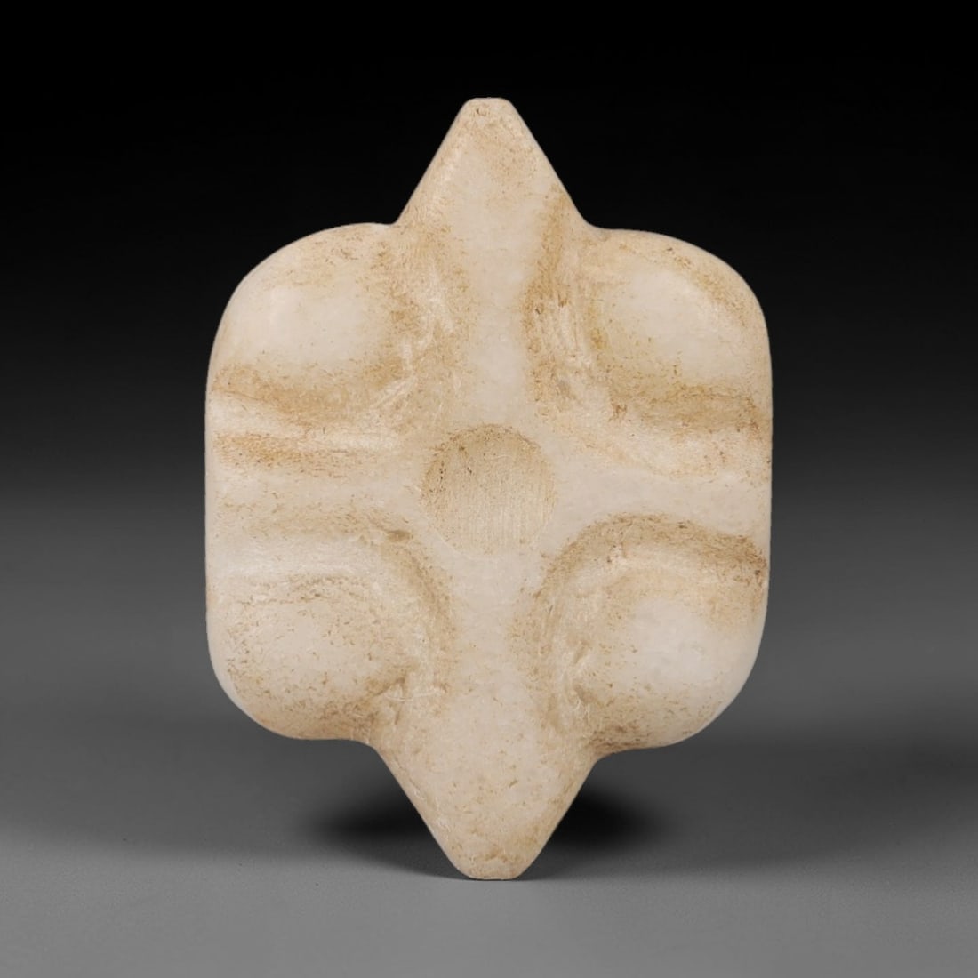 Ancient Marble Amulet - Near Eastern Miniature Relic, 22AK: Crafted from pale marble, this miniature amulet features a symmetrical, four-lobed form with pointed upper and lower terminals. The surface is adorned with four raised, rounded bosses arranged in a cr
