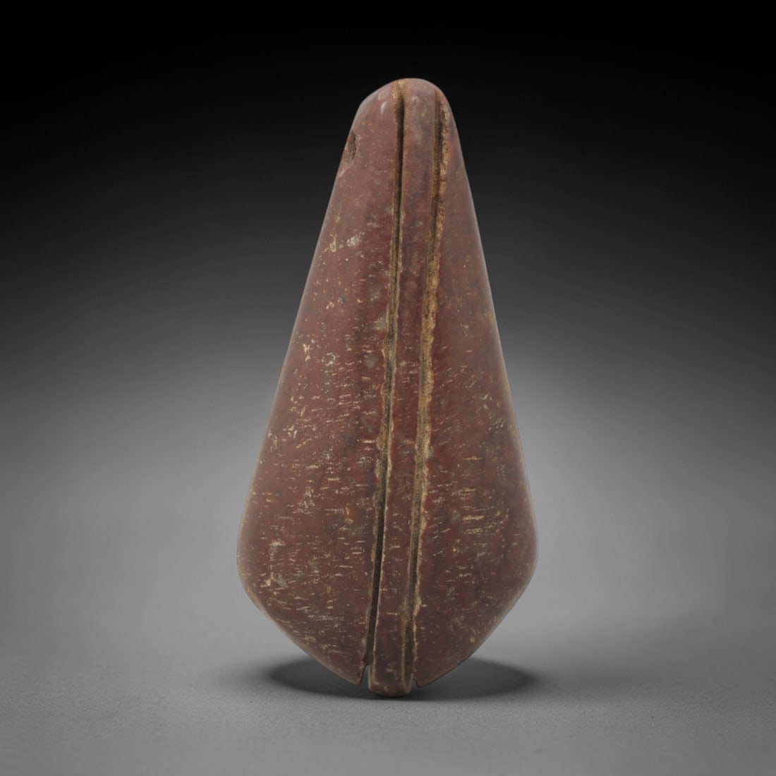 Ancient Stone Leaf Amulet - Egyptian Ritual Pendant, 90XQ: Carved from a dense, reddish-brown stone, this amulet exhibits a teardrop-leaf form with a pointed apex and rounded, slightly indented base. Two parallel incised grooves run vertically along its centr