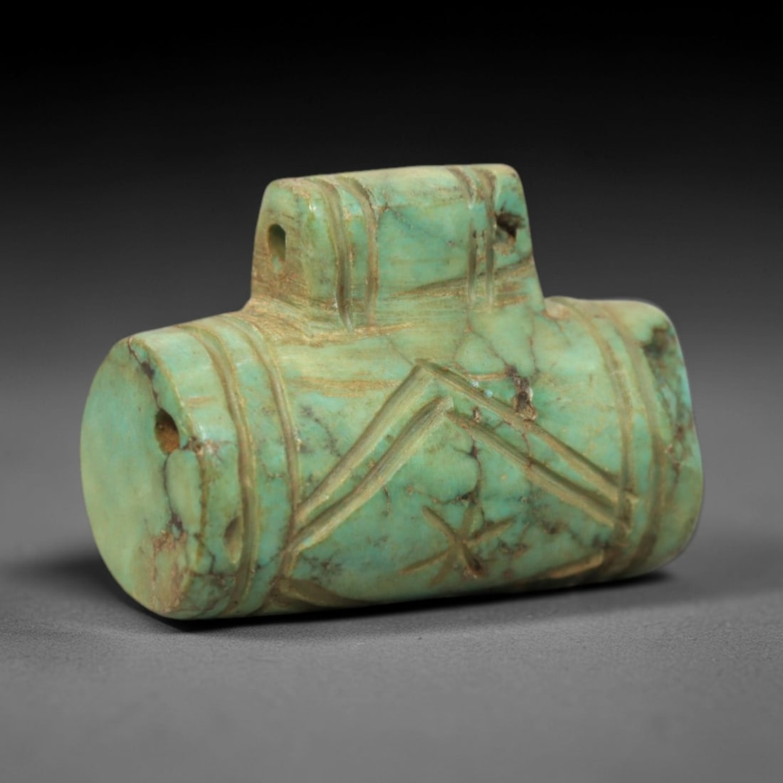 Ancient Turquoise Cylinder Seal - Near Eastern Geometric Amulet, 11XV: Carved from turquoise, this amulet presents a cylindrical form with a raised suspension loop at the top, featuring a central perforation for wear. The body is decorated with incised geometric motifs,