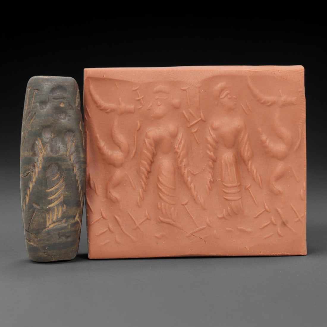 Ancient Steatite Cylinder Seal - Mesopotamian Winged Figures Scene, 81ZR: Carved from dense steatite, this ancient Mesopotamian cylinder seal features a detailed linear relief composition of two winged human figures flanked by animal motifs, executed in the characteristic g