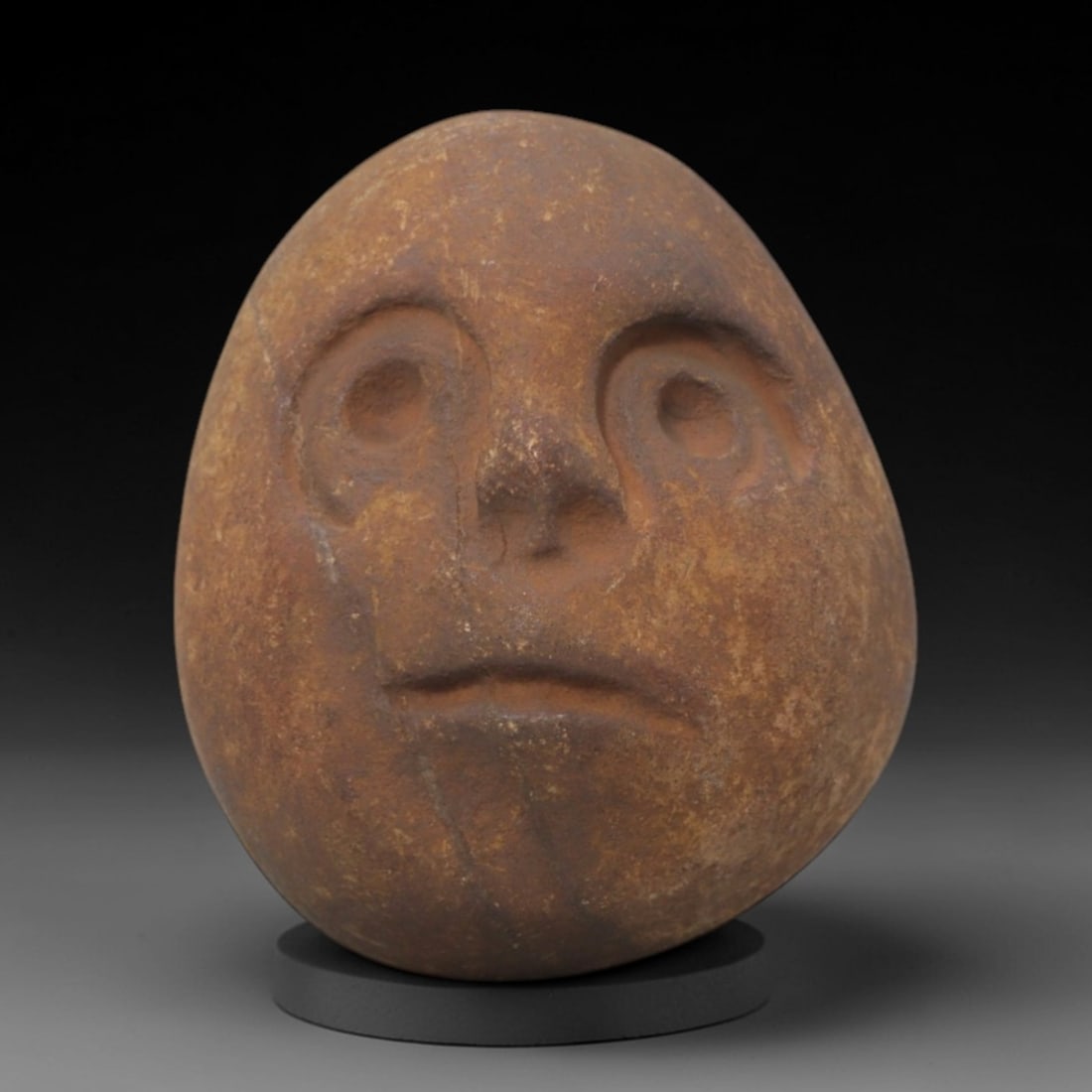 Ancient Stone Anthropomorphic Head - Tribal Ritual Artifact, 74FW: Crafted from compact brown stone, this artifact features a hand-carved anthropomorphic head with deeply incised circular eye sockets, a simplified nasal structure, and a defined mouth, exhibiting the