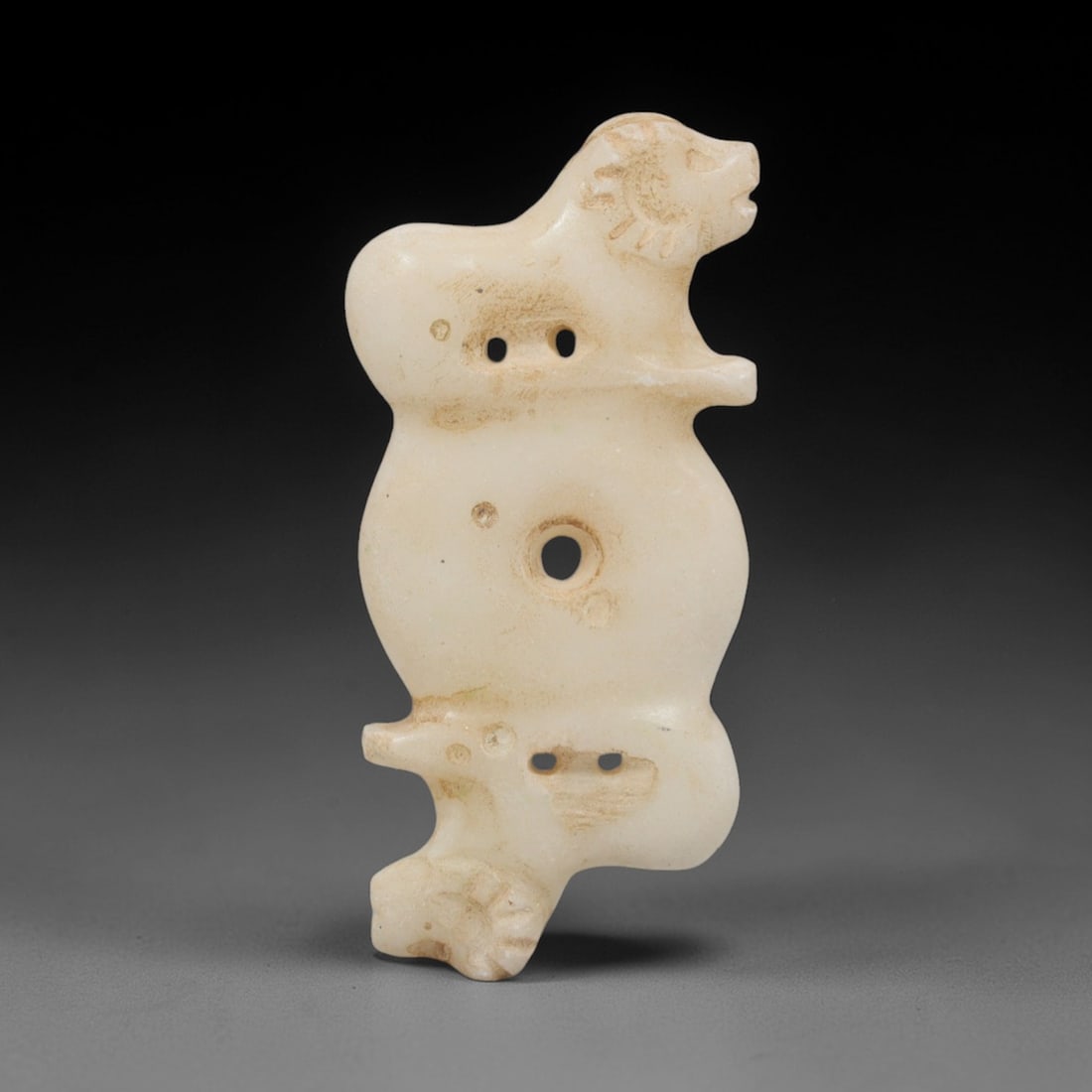 Ancient Marble Double Feline - Near Eastern Amulet Figurine, 96XR: Crafted from pale marble, this amulet features two stylized feline figures positioned at either end of a central, pierced disc. The upper feline is rendered in a reclining posture with incised details