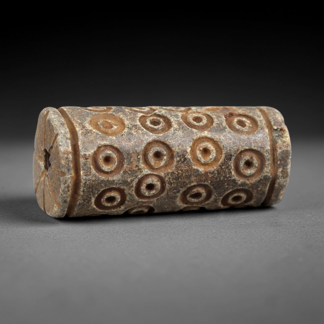 Ancient Steatite Amulet - Near Eastern Concentric Circles, 31AK: Crafted from steatite, this cylindrical amulet features incised concentric circle motifs arranged in horizontal rows across its body, with a radiating linear carving surrounding the suspension hole at