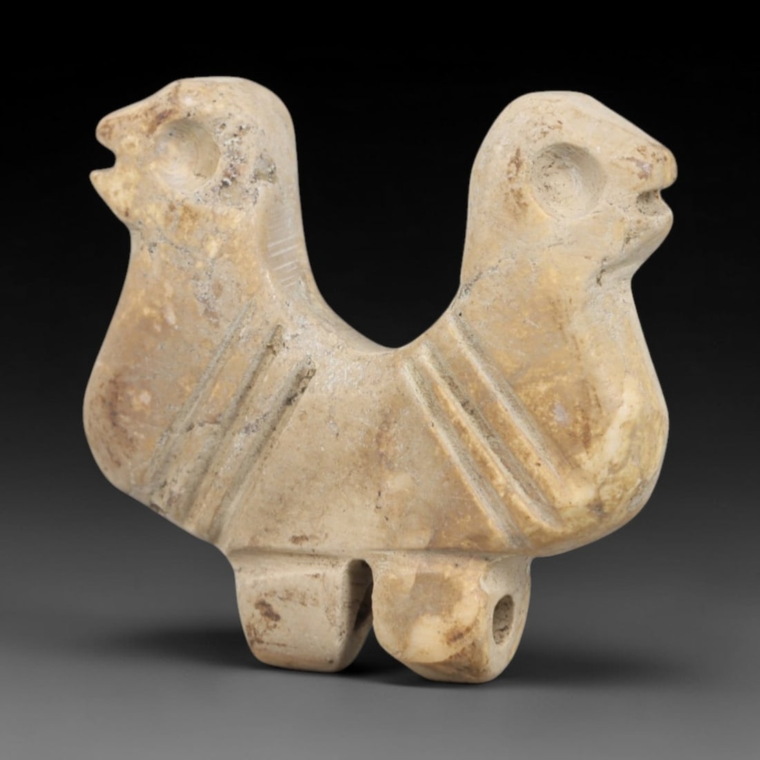 Ancient Steatite Double Bird Amulet - Near Eastern Figurine, 89AR: This artifact is carved from pale, creamy steatite, exhibiting a weathered, matte finish with subtle surface discoloration and mineral variations consistent with age. The form is a symmetrical double