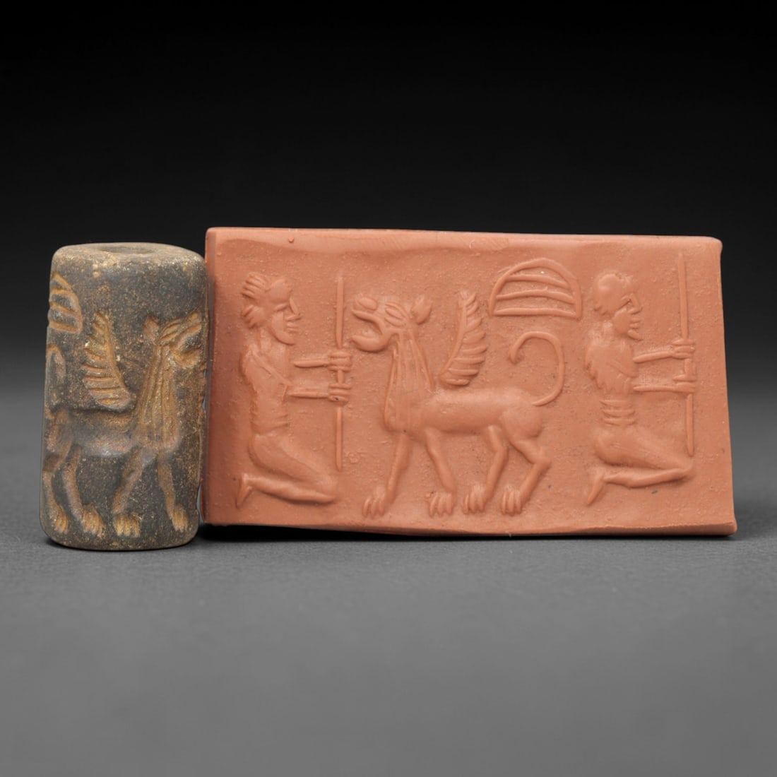 Ancient Steatite Cylinder Seal - Mesopotamian Griffin & Kneeling Attendants Scene, 16ZP: Carved from dark, granular steatite, this ancient Mesopotamian cylinder seal depicts a powerful apotropaic scene, executed with precise glyptic craftsmanship characteristic of the Late Bronze Age. The