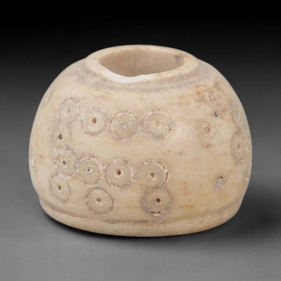 Ancient Near Eastern Bone Spindle Whorl - Dot-in-Circle Motif, 91AH: Carved from ancient bone, this Near Eastern spindle whorl features a continuous dot-in-circle motif encircling its central perforation, a design with apotropaic significance in ancient Near Eastern cu