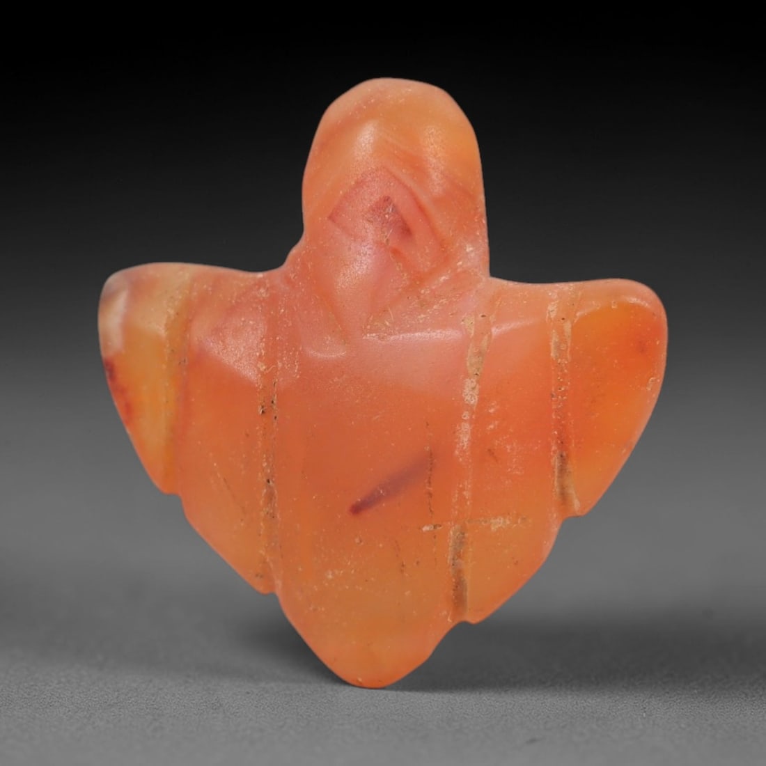 Ancient Carnelian Bird Amulet - Egyptian Figurine, 51AJ: Carved from translucent orange carnelian, this amulet is shaped into a stylized avian form with outstretched wings and a pointed lower body, consistent with ancient Egyptian protective amulet traditio
