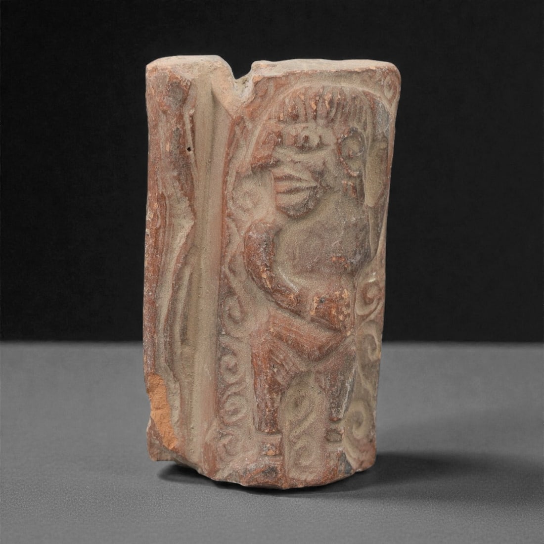 A Near Eastern Terracotta Plaque, 3rd-2nd Millennium BCE, 81FL: Molded from reddish-brown terracotta with natural surface patination and visible edge losses, the object is formed as a rectangular plaque fragment. The relief depicts a standing humanoid figure with