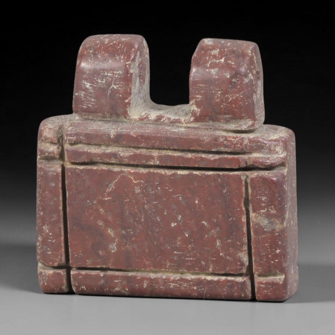 Ancient Stone Double-Headed Amulet - Near Eastern Figurine, 63AP: Carved from a rich, reddish stone with natural mineral inclusions and weathered patina, this amulet features a rectangular, segmented body topped with two rounded, stylized heads. Each head bears subt