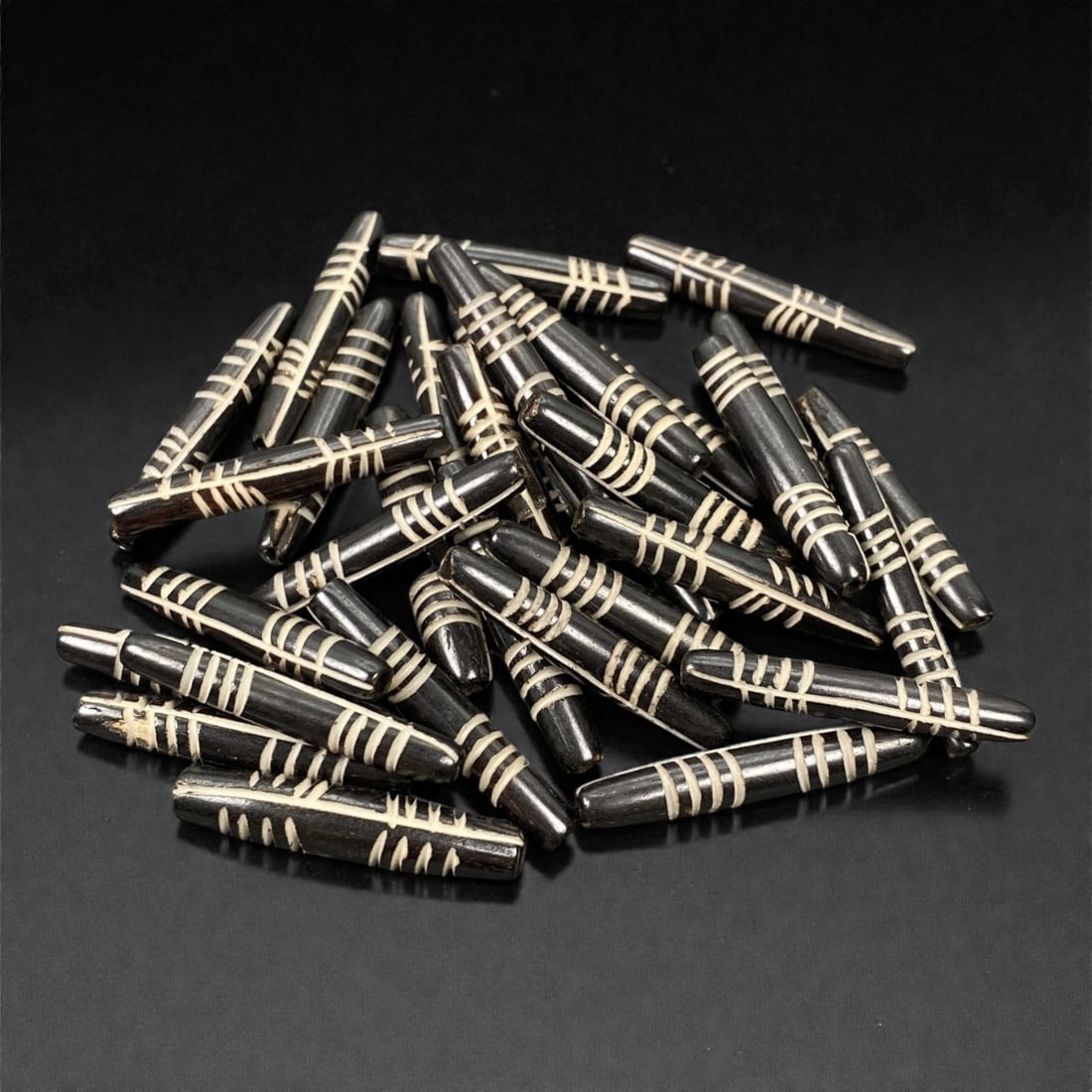 A Tibetan Bone Bead Group, Inlaid Banded Pattern, 20th Century, 87S: Composed of animal bone, each bead features an elongated cylindrical form with a tapered end, consistent in length and diameter across the group. The surface displays an inlaid banded pattern, with wh