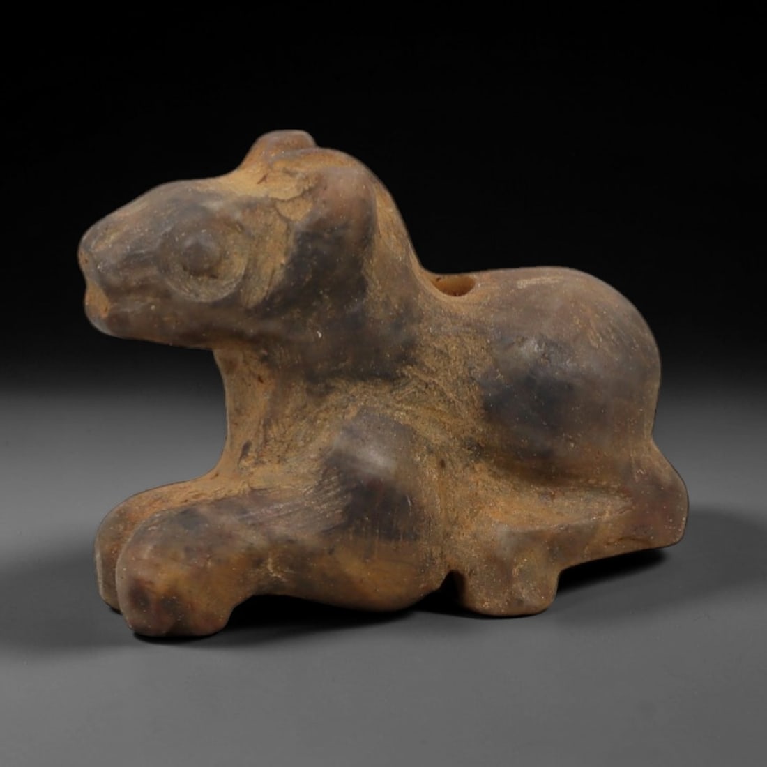 Ancient Speckled Stone Recumbent Feline - Near Eastern Amulet, 94AD: Carved from mottled brown-and-tan speckled stone, this amulet depicts a recumbent feline in a compact, stylized form. The creature is rendered in a prone resting posture, with simplified facial featur