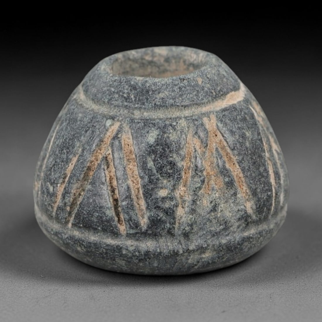 Ancient Bone Spindle Whorl - Near Eastern Triangular Motif, 87XR: This ancient Near Eastern spindle whorl is carved from bone, featuring a convex form with a central perforation. The surface is incised with triangular and linear motifs, a common decorative technique