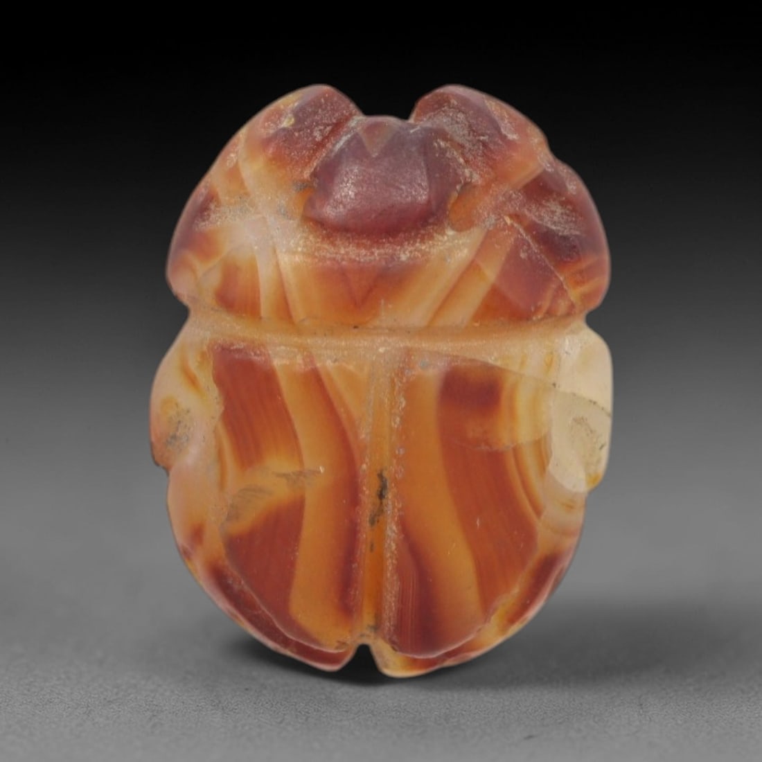 Ancient Agate Scarab - Egyptian Amulet Bead, 62XS: This amulet is carved from banded orange-red agate, exhibiting striking natural banding and a smooth, polished finish characteristic of ancient Egyptian glyptic craftsmanship. The form is a classic sc