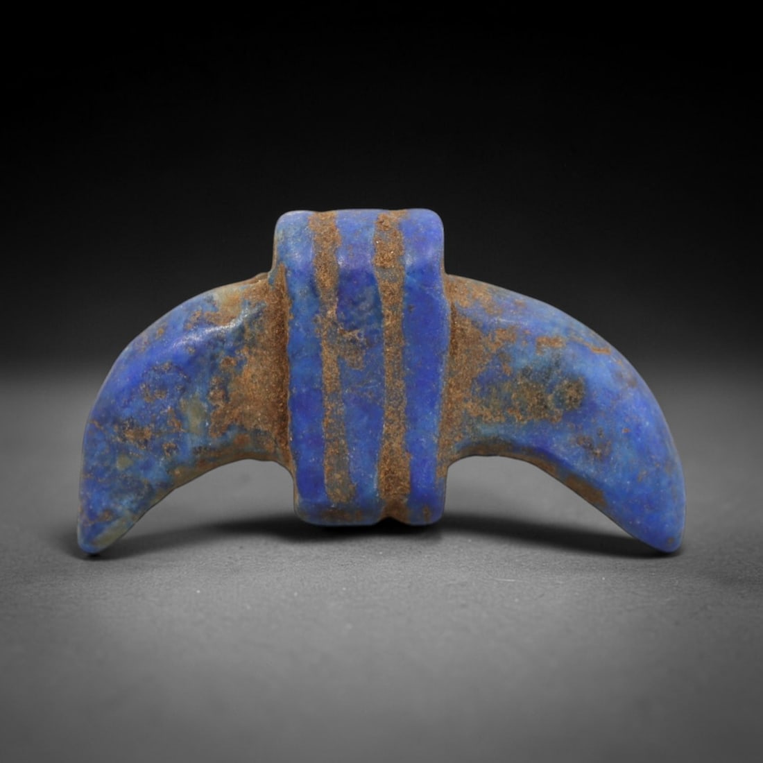 Ancient Lapis Lazuli Amulet - Egyptian Double Crescent Pendant, 32ZT: Carved from lapis lazuli, this amulet features a symmetrical double-crescent form with a rectangular central block pierced for suspension, its surface incised with three vertical bands that define its