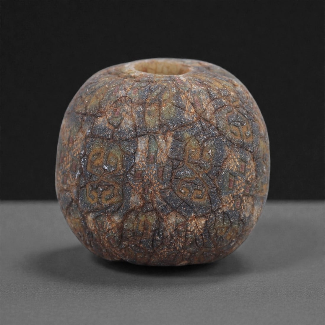 Ancient Glass Bead - Roman Mosaic Cane Sphere, 70J: Formed from intricately fused mosaic canes, this bead exhibits a dense, tessellated arrangement of small geometric elements in muted tones of red, blue, and yellowish beige. The patterning is characte
