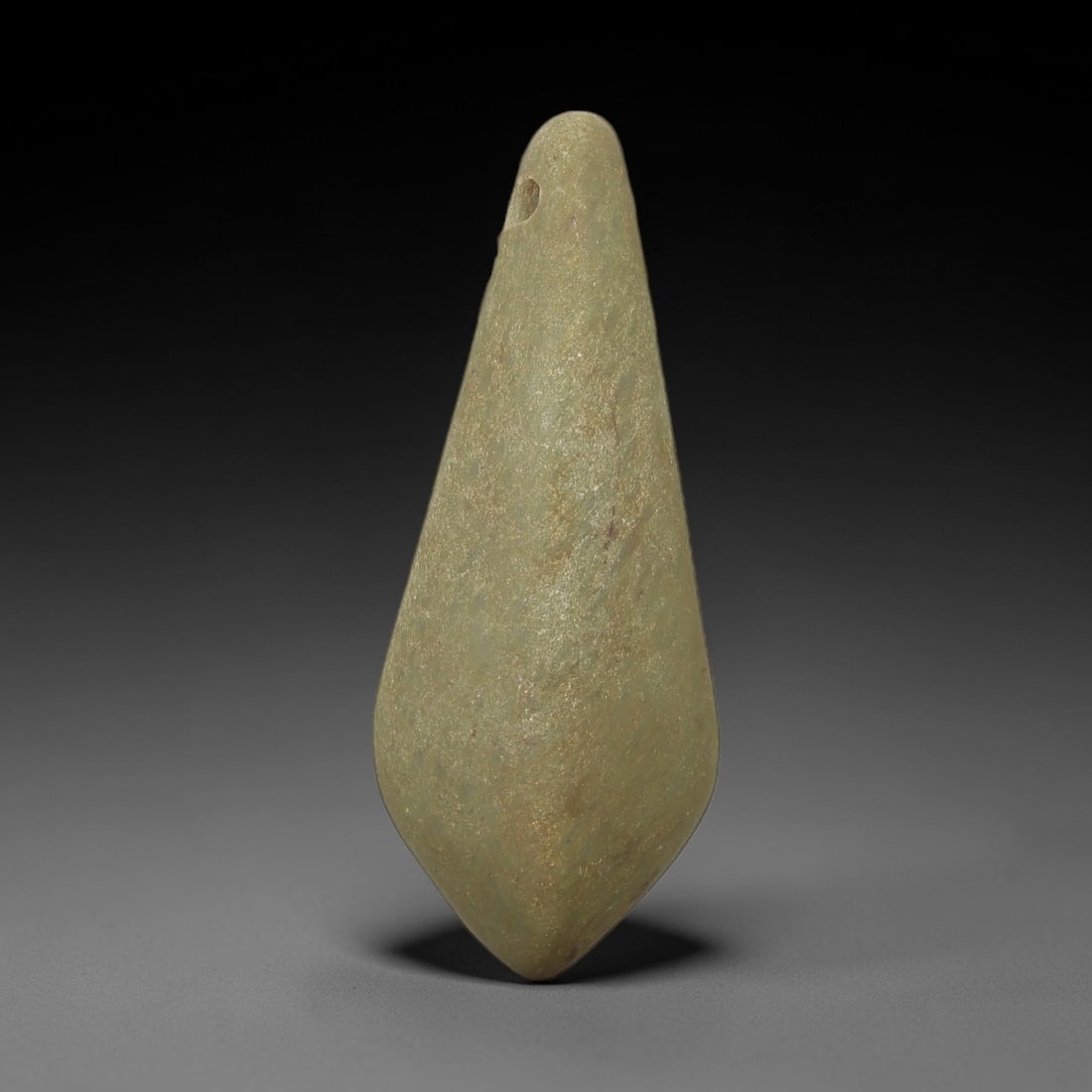 Ancient Green Stone Teardrop Amulet - Near Eastern Pendant, 43AE: This artifact is a carved green stone teardrop amulet of Near Eastern origin, fashioned from a mottled olive-green stone with subtle mineral veining and a fine, granular texture. Its elongated, symmet