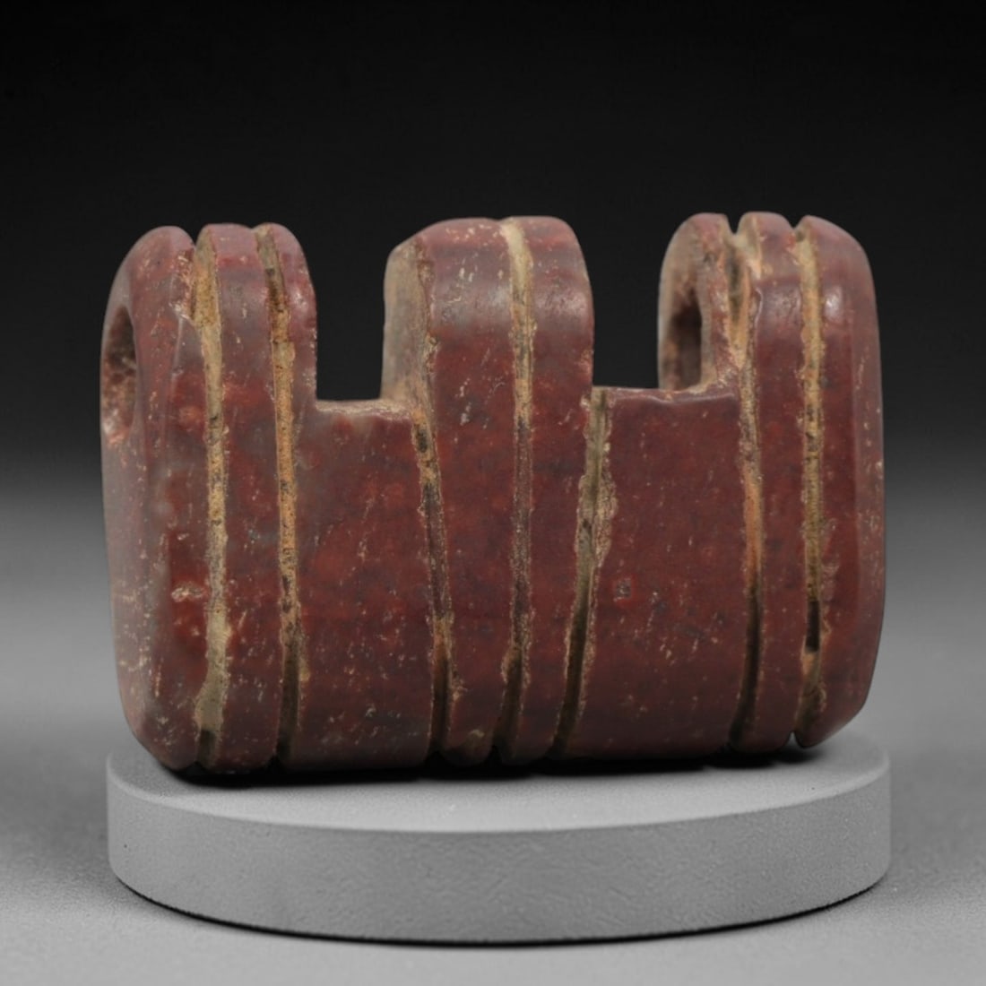 Ancient Near Eastern Red Stone Triple Amulet - Carved Bead, 31ZV: This amulet is carved from a rich, deep red stone with natural speckling, likely brecciated jasper or red steatite, featuring a symmetrical triple-form design. The piece is composed of three adjacent