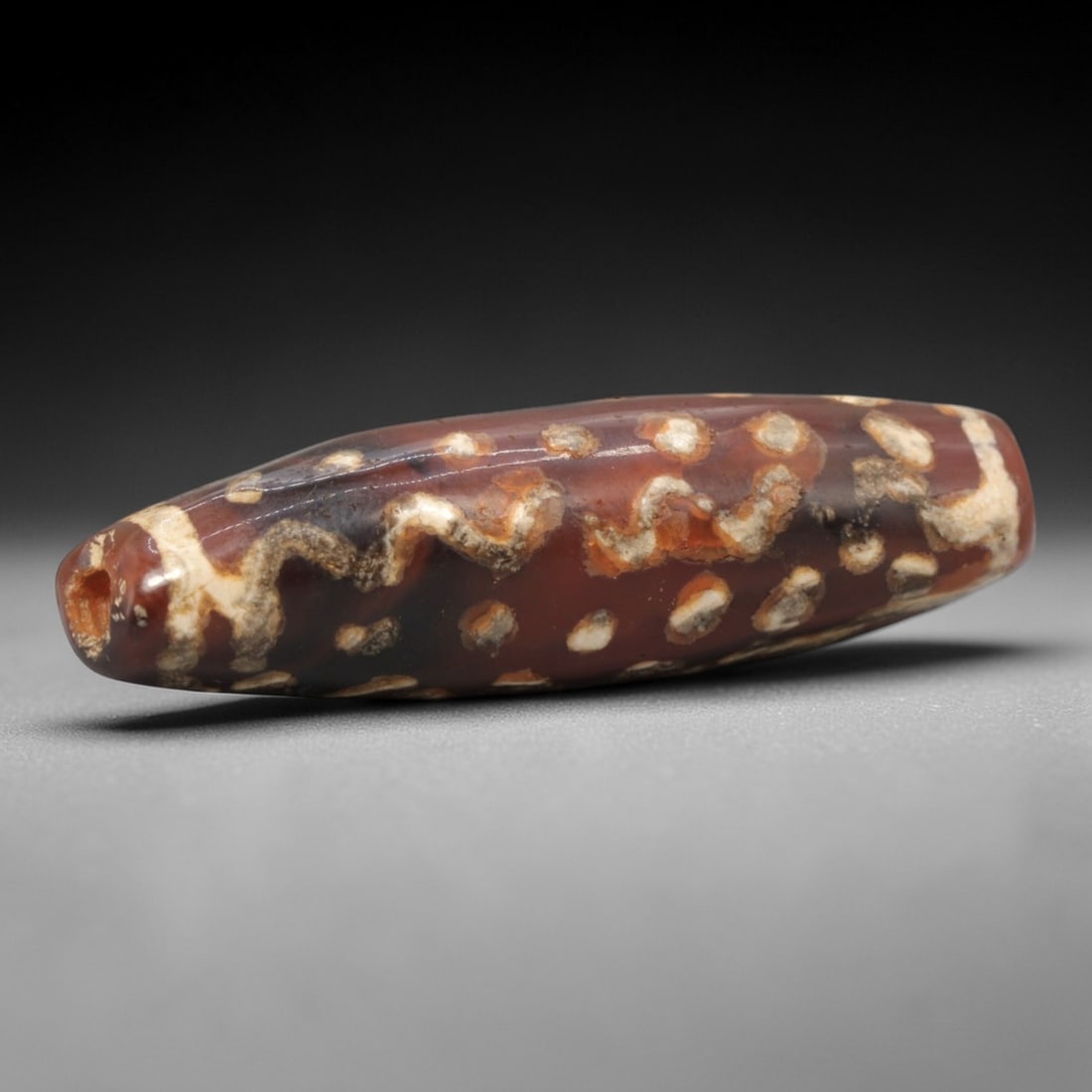 Ancient Carnelian Etched Dzi Bead - Himalayan Amulet, 63XV: Crafted from rich carnelian, this bead features intricate etched white patterns including wavy linear motifs and circular dot motifs, executed in the traditional Himalayan Dzi bead craftsmanship. The