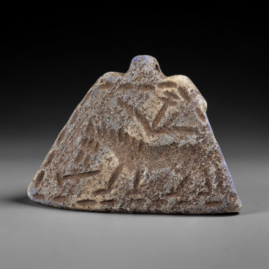 Ancient Lapis Lazuli Amulet - Near Eastern Zoomorphic Figurine, 21FY: Carved from weathered lapis lazuli, this triangular amulet features a zoomorphic form with incised linear and geometric motifs across its surface, alongside a small perforation at the apex for suspens