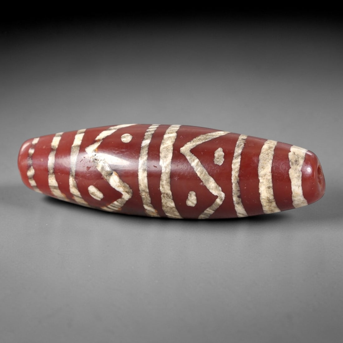 Ancient Carnelian Dzi Bead - Himalayan Etched Amulet, 15AS: This ancient elongated bead is crafted from polished carnelian, featuring a rich reddish-brown base with crisp white etched geometric motifs, including triangular and linear banding patterns. The bead