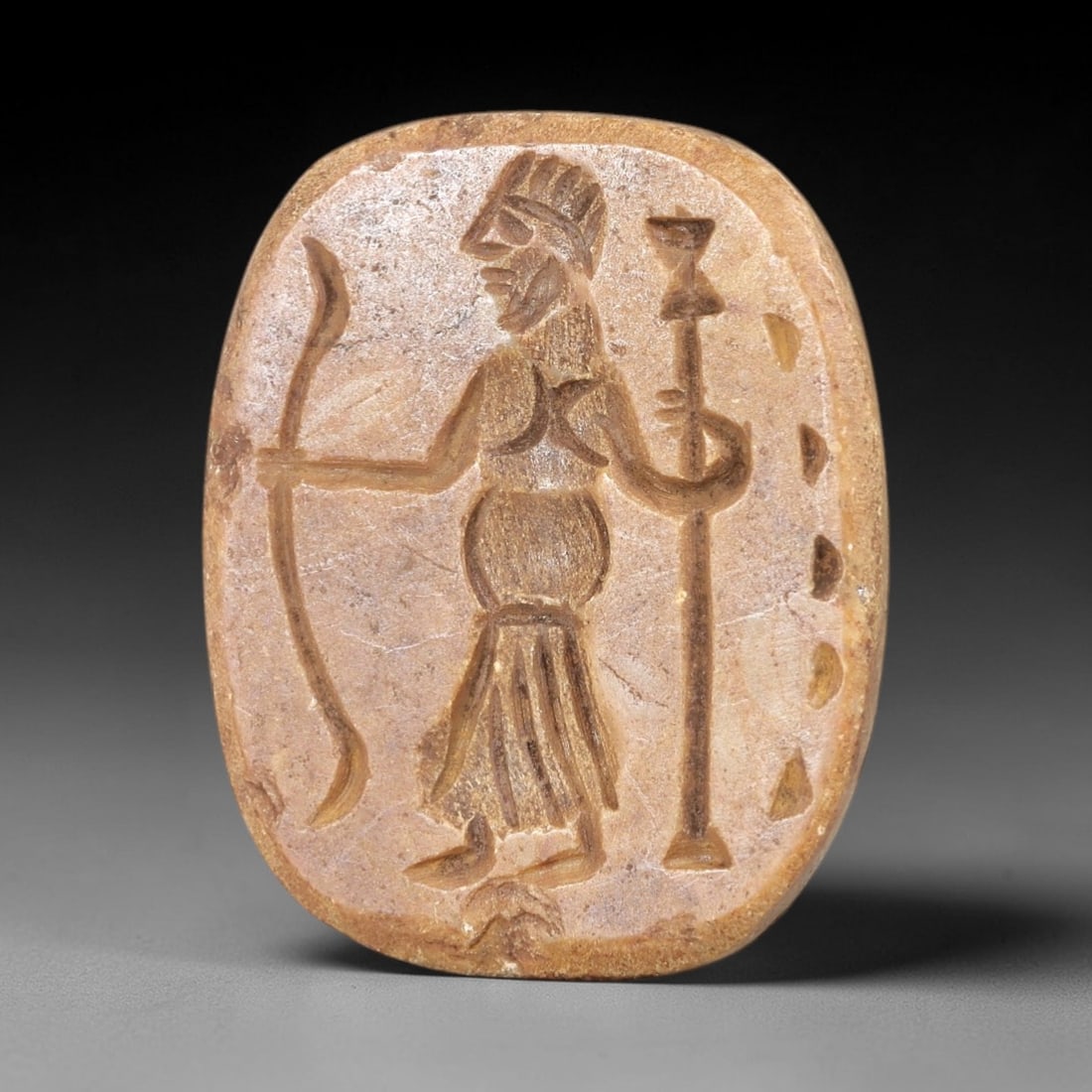 Ancient Steatite Stamp Seal - Near Eastern Warrior Figurine, 51AS: This ancient Near Eastern stamp seal is carved from steatite, formed as an oval plaque with incised decoration depicting a standing warrior figure in profile, holding a bow in one hand and a tall scep