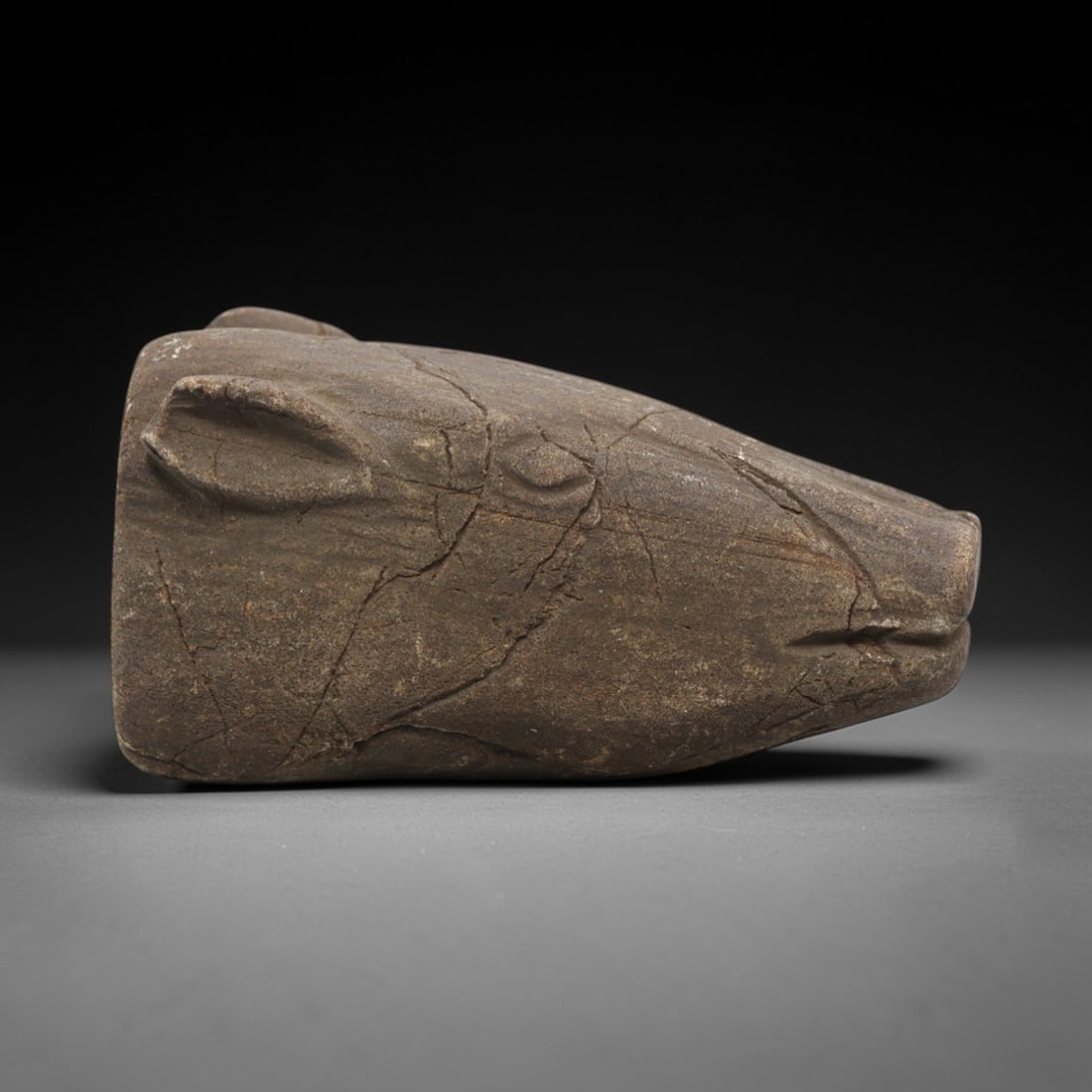 Ancient Stone Zoomorphic Head - Near Eastern Animal Carving, 82ZV: This artifact is a carved stone zoomorphic head, crafted from a granular, earth-toned stone consistent with ancient Near Eastern lithic traditions. The relief carving depicts a stylized animal head, l