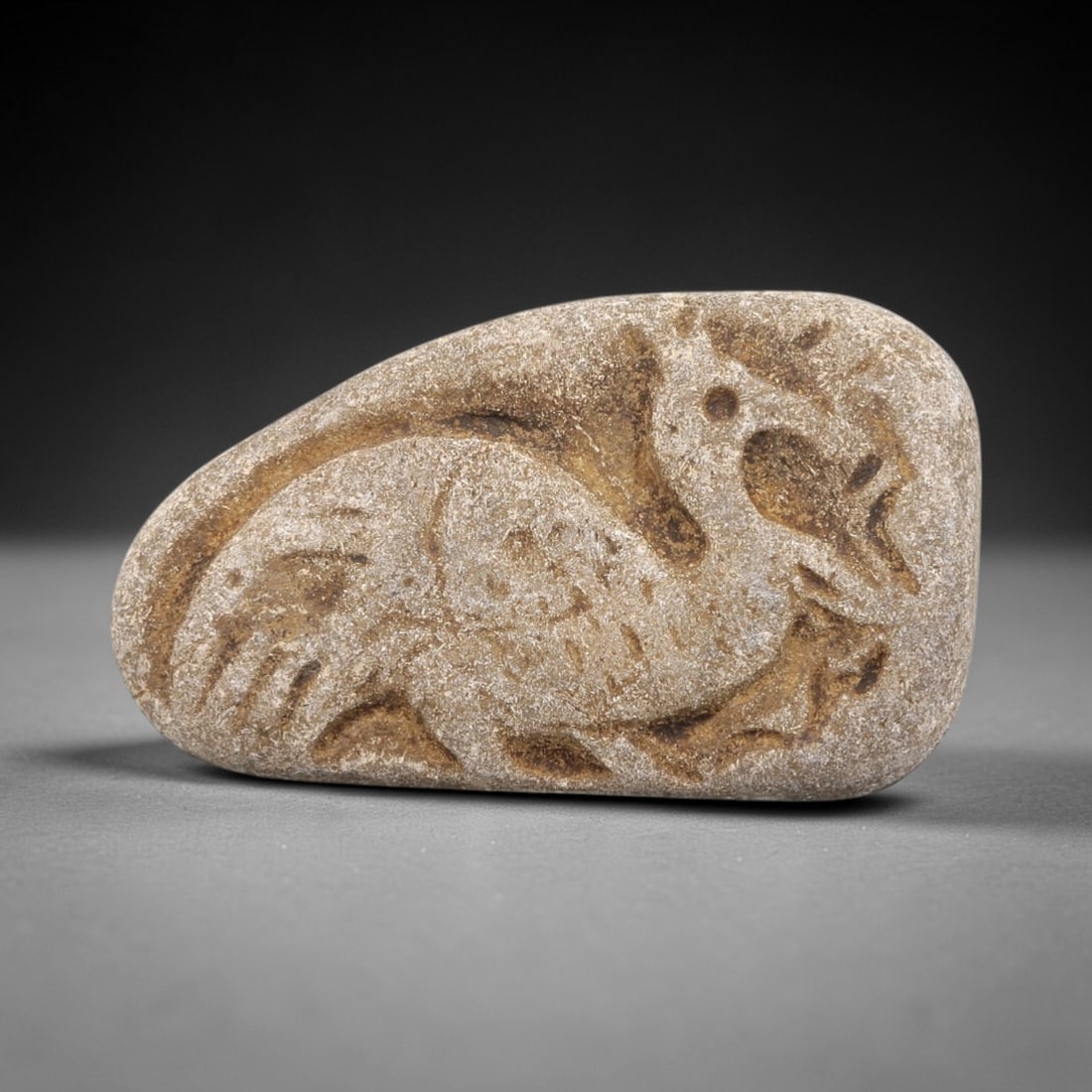 Ancient Stone Bird Amulet - Near Eastern Christian Figurine, 99FX: Carved from a naturally smoothed stone pebble, this piece features a relief depiction of a bird in crouched pose, with incised details defining its wings, body, facial features, and clawed limbs. Styl