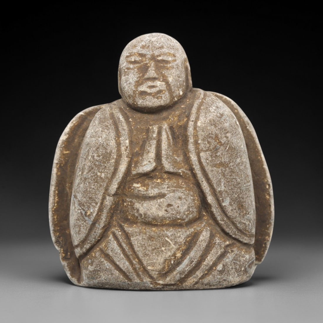 Edo Period Stone Monk - Japanese Antique Figurine, 84ZV: Carved from a weathered stone, this figurine depicts a seated Edo period Buddhist monk in a meditative pose with hands clasped in prayer, with incised lines defining the flowing robes, rounded belly,