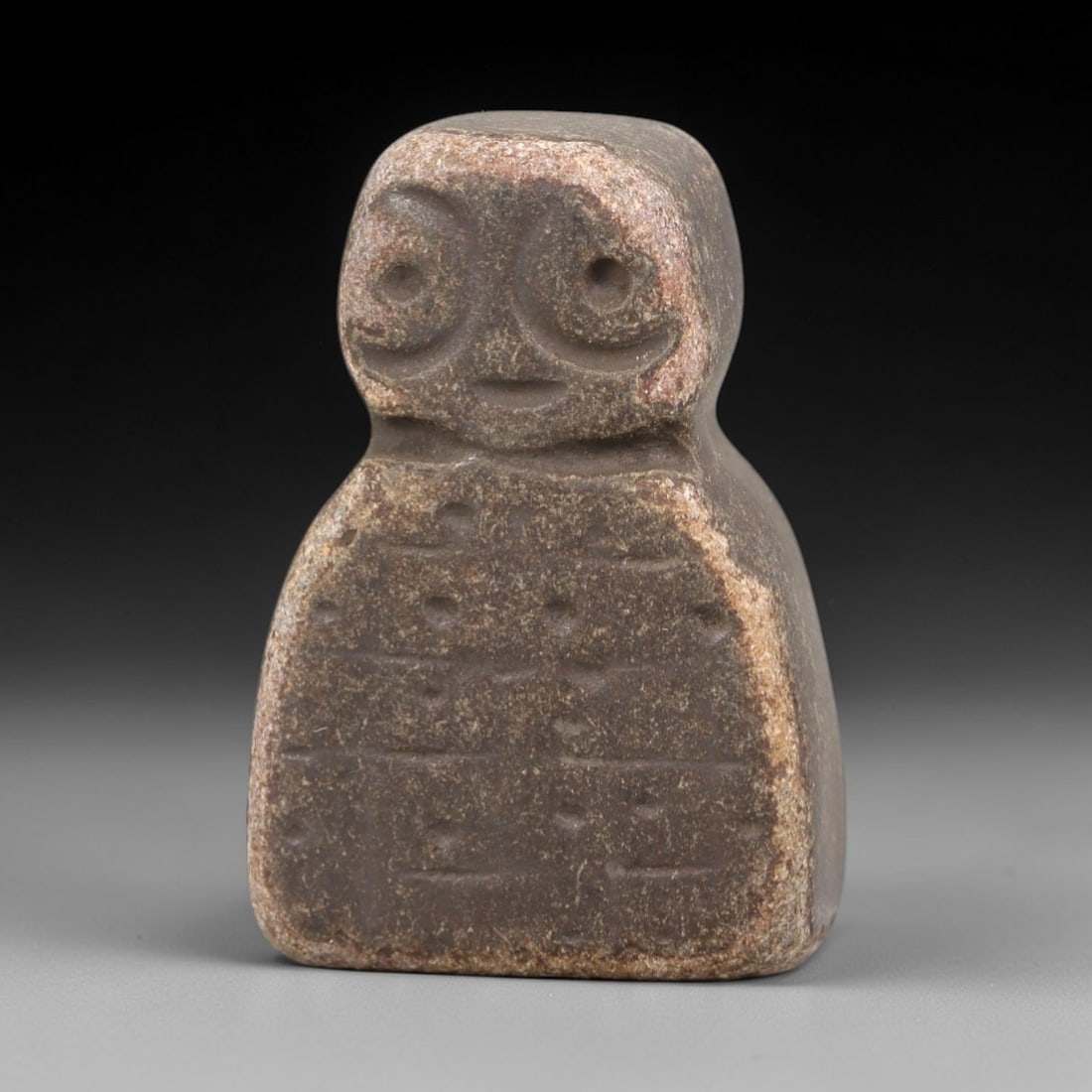 Ancient Stone Idol - Near Eastern Figurine, 16FY: Carved from a compact, bell-shaped stone, this idol features a stylized head with large circular eyes and a simple smiling mouth, paired with a rectangular body incised with geometric dot-and-line mot