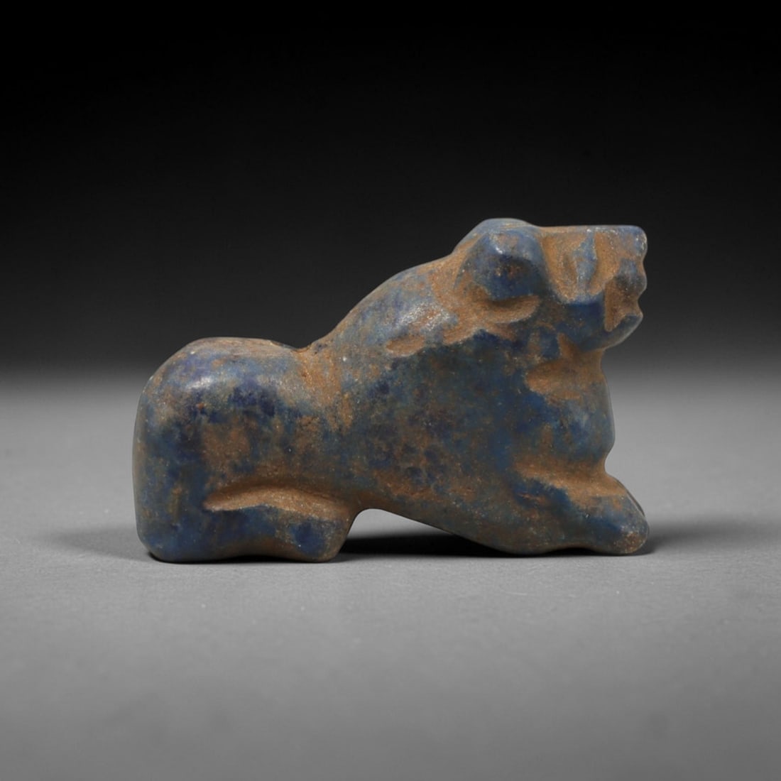 Ancient Lapis Lazuli Feline - Near Eastern Amulet Figurine, 98XV: Carved from lapis lazuli, this amulet depicts a recumbent feline in a stylized, compact form. The head is defined with incised eye and snout detailing, small rounded ears, and a robust neck, while the