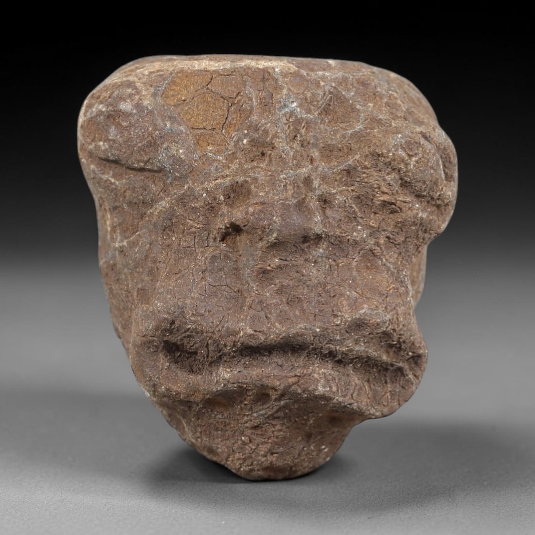 Ancient Stone Maskette - Medieval Figurine, 19FY: Carved from a rough, naturally textured stone, this maskette features a simplified, stylized facial form with incised details defining the eyes, nose, and mouth. Stylistically consistent with medieval