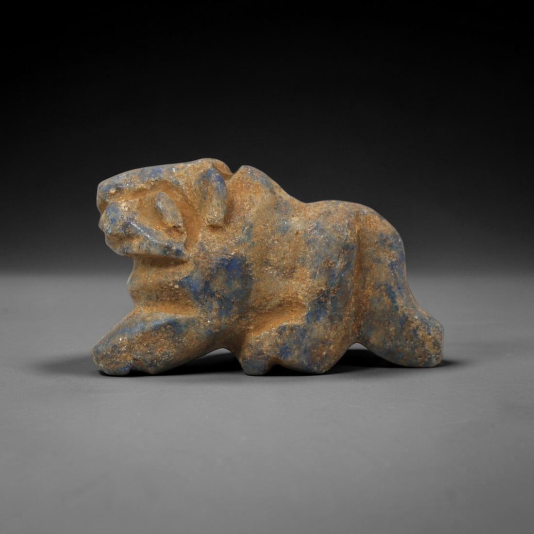 Ancient Lapis Lazuli Feline - Near Eastern Amulet Figurine, 10XT: Carved from lapis lazuli, this amulet depicts a crouched feline in a predatory stance with angular, stylized features. The head is defined with incised eye and snout detailing, small upright ears, and