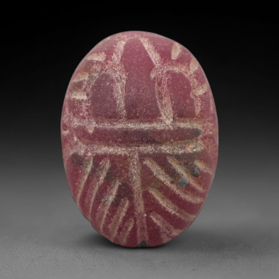 Ancient Glass Scarab - Egyptian Amulet Bead, 60XS: This amulet is crafted from opaque deep red glass, emulating the appearance of carnelian, a practice common in ancient Egyptian and Near Eastern glyptic traditions. The form is a classic scarab beetle