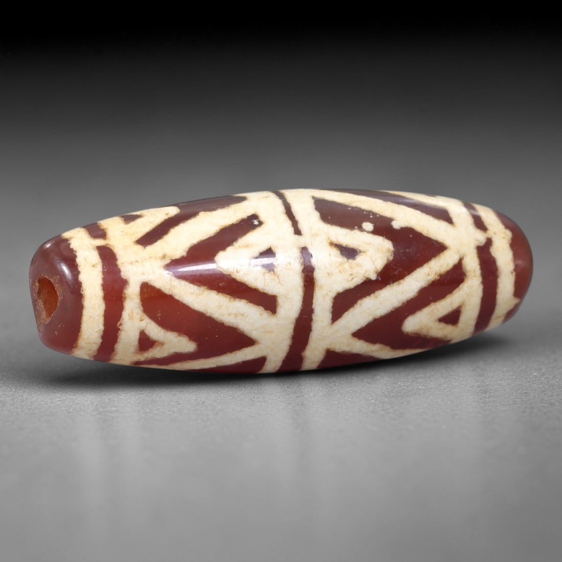 Ancient Carnelian Dzi Bead - Himalayan Geometric Amulet, 3AS: This ancient elongated bead is crafted from polished carnelian, featuring a rich reddish-brown base with intricate white etched interlocking geometric motifs across its surface. The bead retains a fin