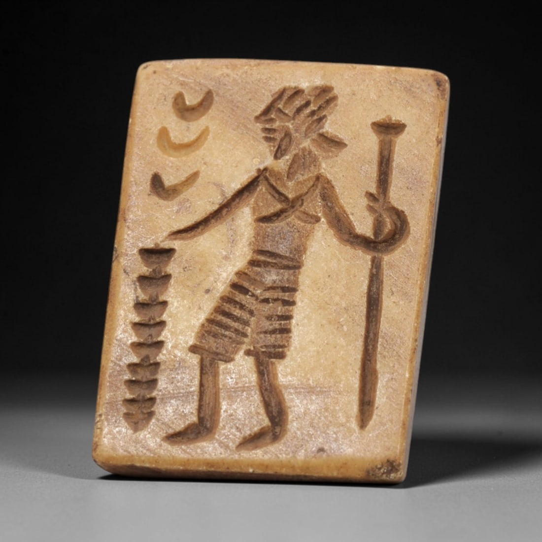 Ancient Steatite Stamp Seal - Near Eastern Anthropomorphic Figurine, 99ZV: This ancient Near Eastern stamp seal is carved from steatite, formed as a rectangular plaque with incised decoration depicting a standing anthropomorphic figure in profile, holding a tall staff in one