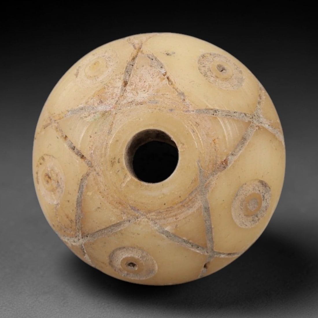 Ancient Near Eastern Bone Spindle Whorl - Dot-in-Circle Motif, 2AJ: Carved from ancient bone, this Near Eastern spindle whorl features a continuous dot-in-circle motif encircling its central perforation, a design with apotropaic significance in ancient Near Eastern cu