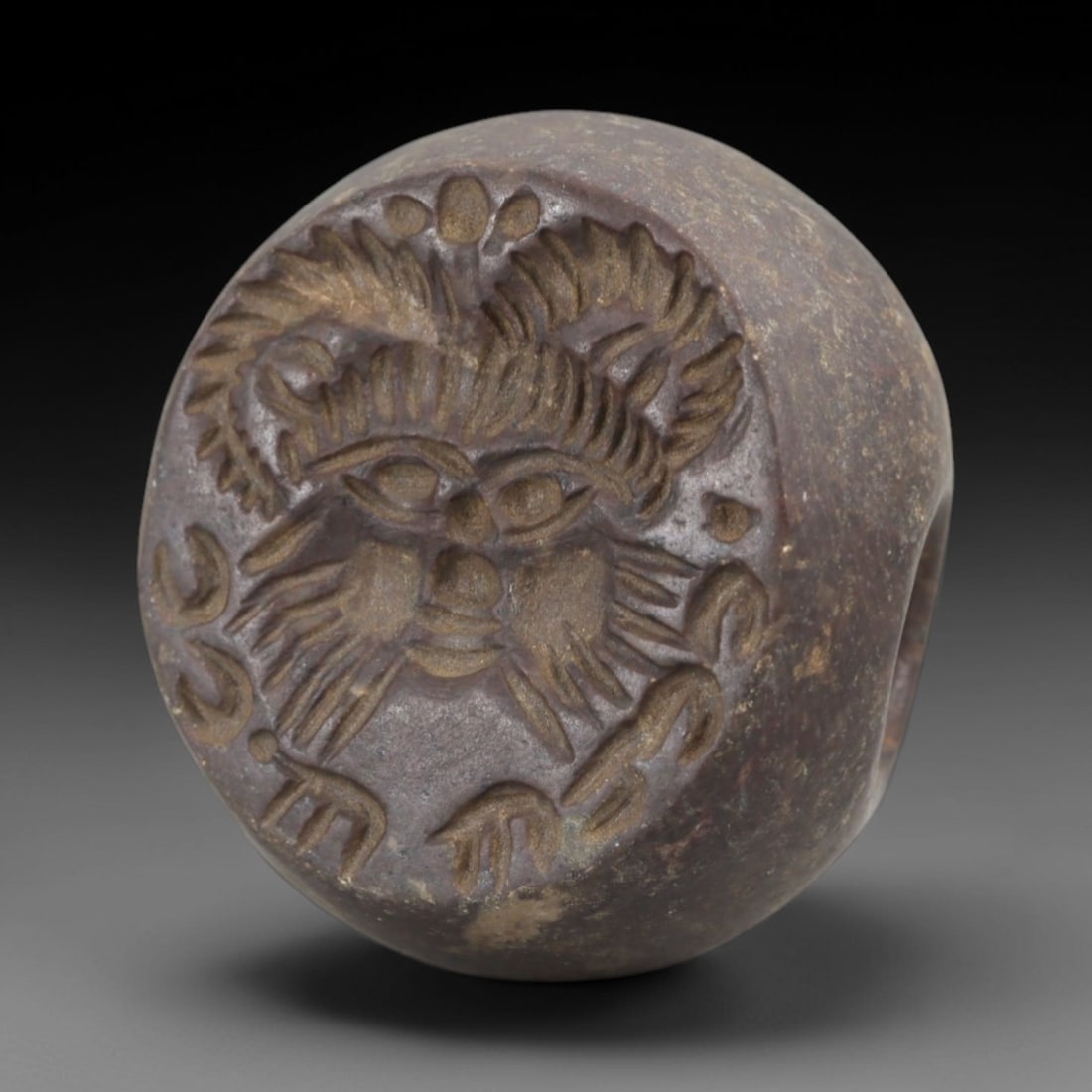Ancient Steatite Stamp Seal - Sasanian Anthropomorphic, 48AK: Carved from steatite, this hemispherical Sasanian stamp seal features a central anthropomorphic face motif with stylized horns, facial hair, and expressive features, surrounded by incised epigraphic s
