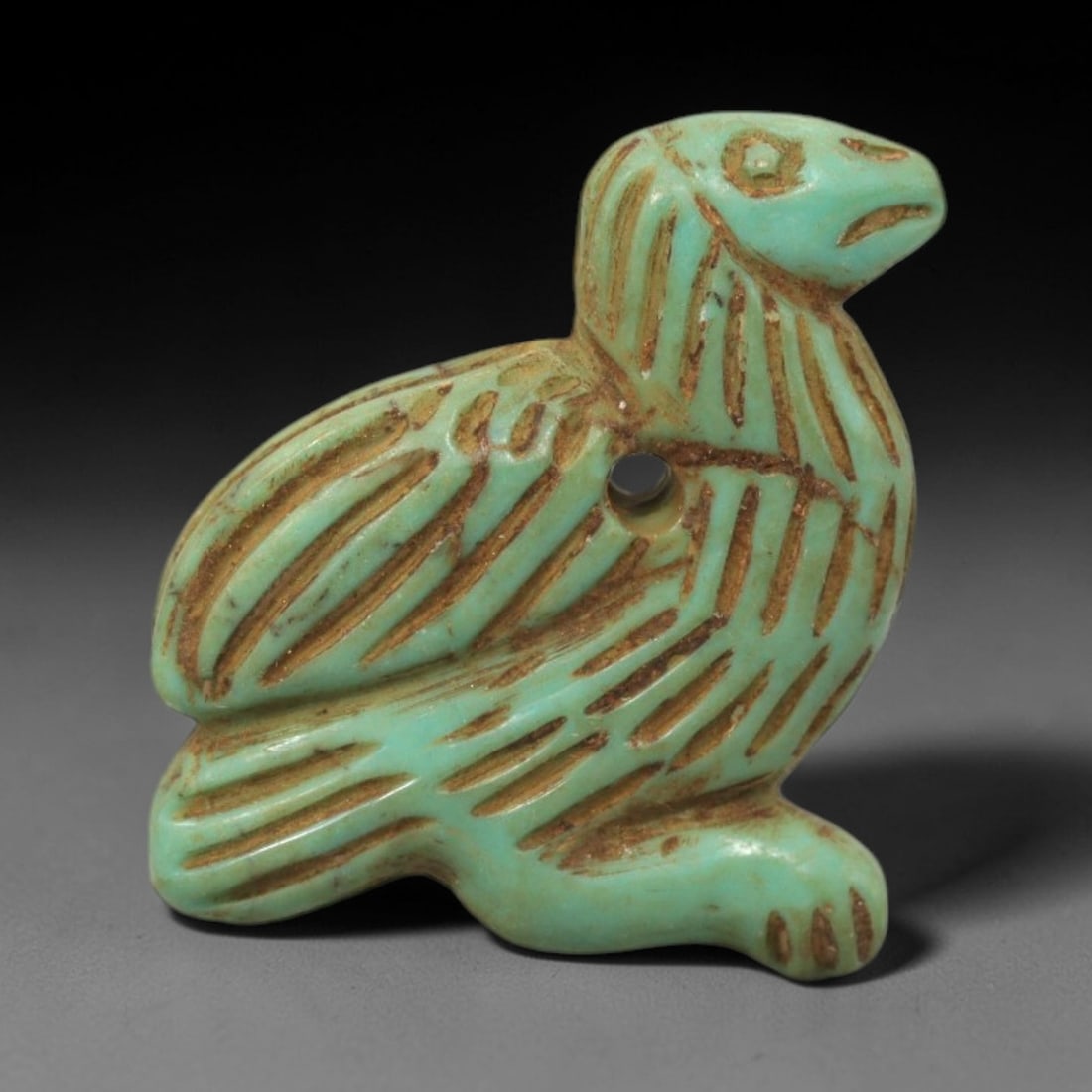 Ancient Turquoise Bird Amulet - Near Eastern Figurine, 2XV: Carved from turquoise, this amulet takes the form of a stylized bird with incised linear striations detailing the wings and body, and a distinct circular eye motif. A perforation through the torso ind